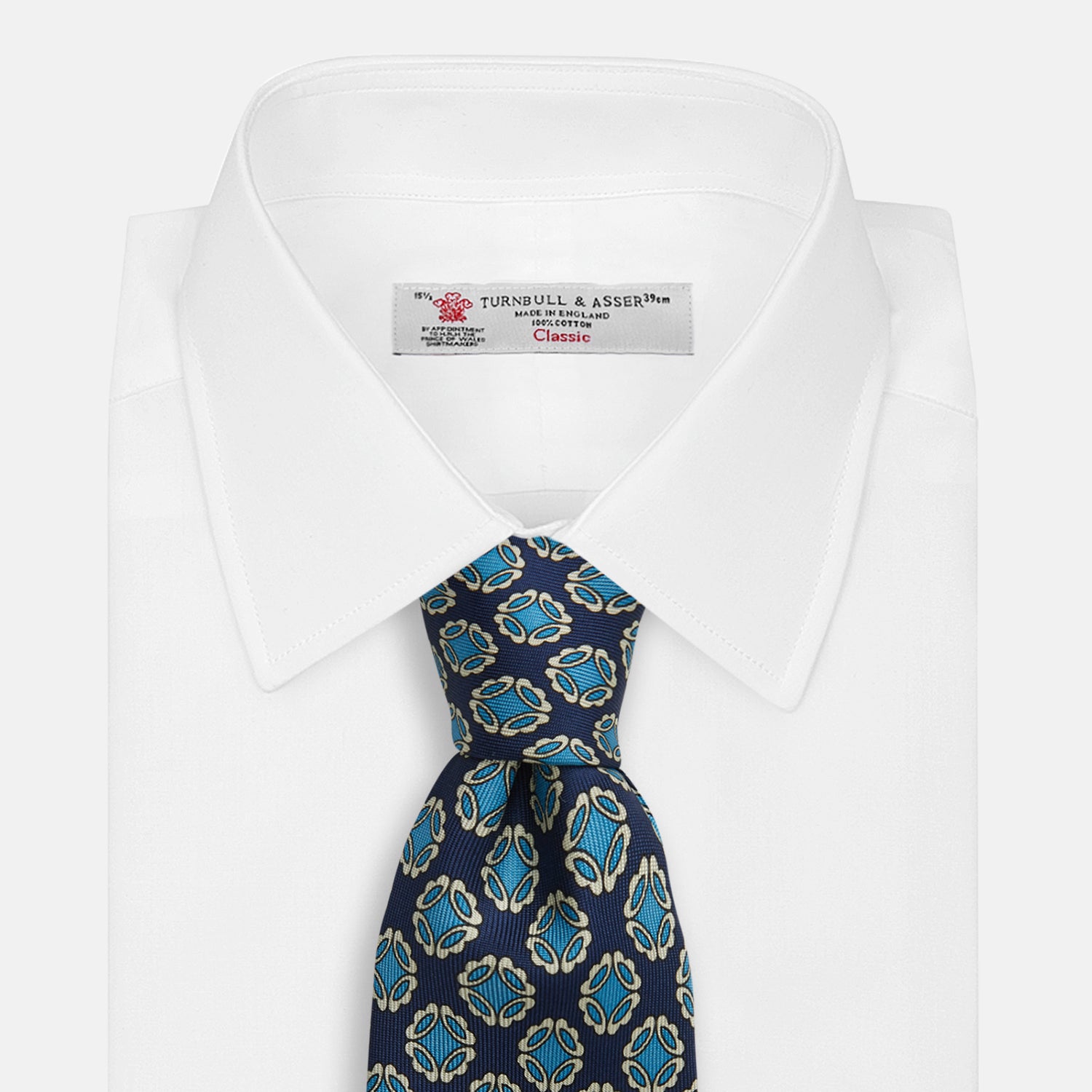 View 2 of product A rolled Navy Floral Geometric Tie by Turnbull & Asser, shown on a light background with light blue and white geometric floral motifs—a refined, stylish accessory.