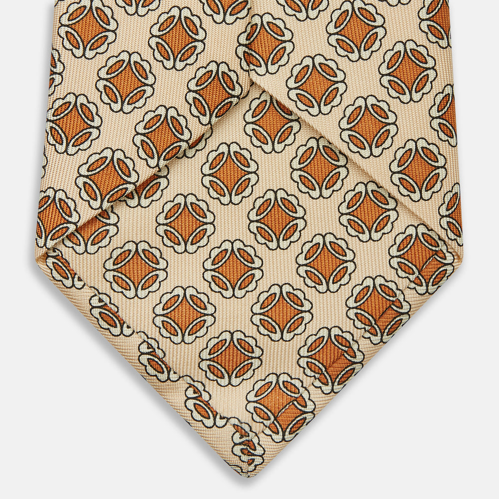A cream floral geometric tie by Turnbull & Asser, rolled with the pointed end forward, is displayed on a white background.