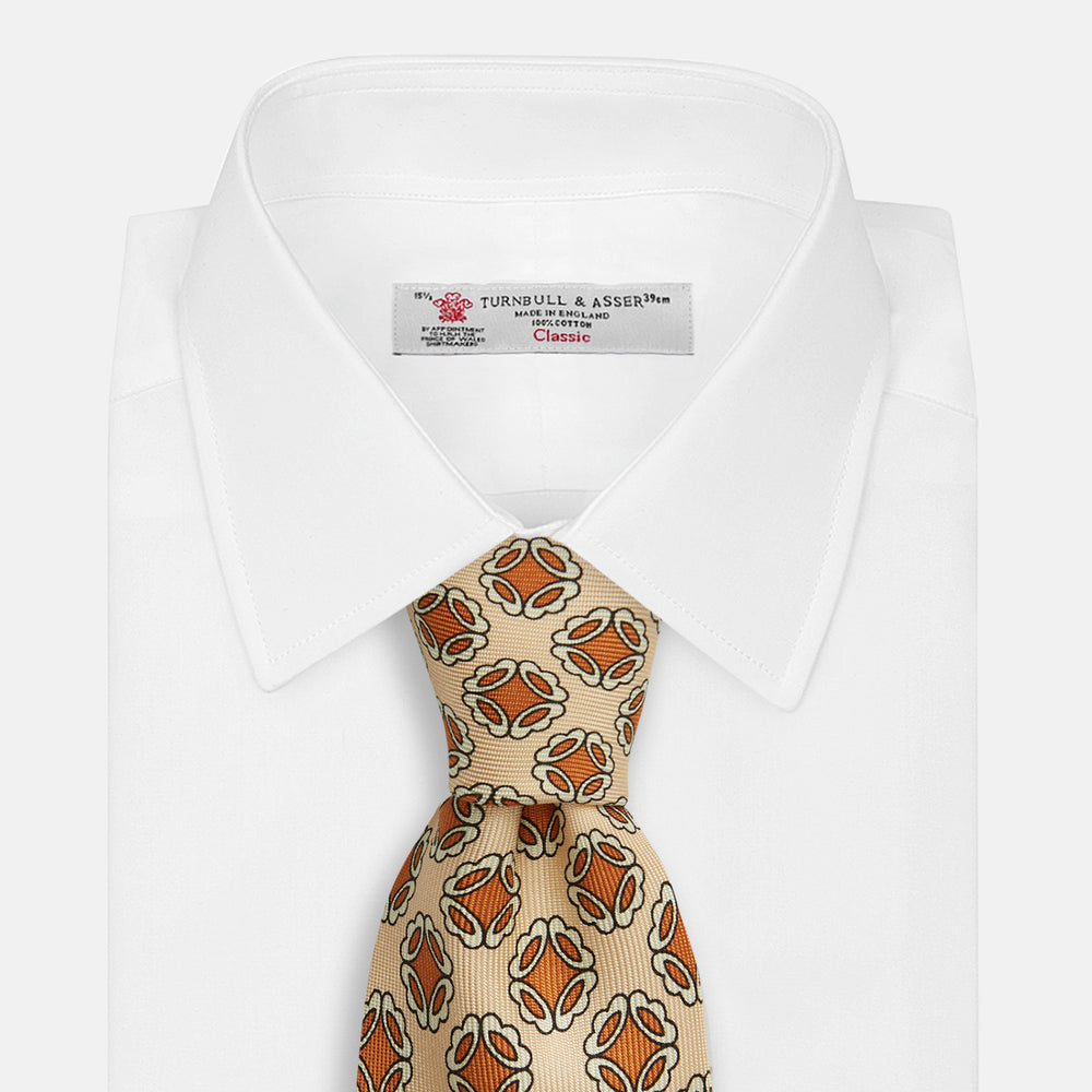 A cream floral geometric tie by Turnbull & Asser, rolled with the pointed end forward, is displayed on a white background.