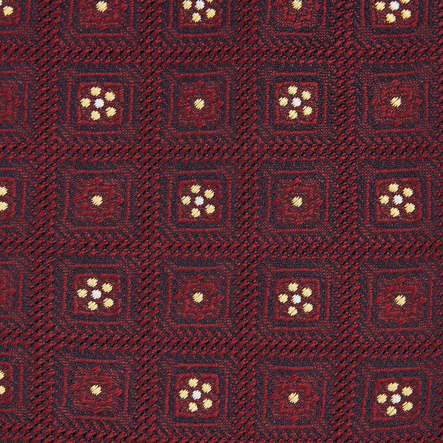View 3 of product The Turnbull & Asser Burgundy Illusion Flower Silk Tie features a geometric pattern of small yellow and white dots within diamond shapes, elegantly displayed rolled up on a light background.