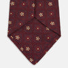 View 4 of product The Turnbull & Asser Burgundy Illusion Flower Silk Tie features a geometric pattern of small yellow and white dots within diamond shapes, elegantly displayed rolled up on a light background.