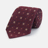 View 1 of product The Turnbull & Asser Burgundy Illusion Flower Silk Tie features a geometric pattern of small yellow and white dots within diamond shapes, elegantly displayed rolled up on a light background.