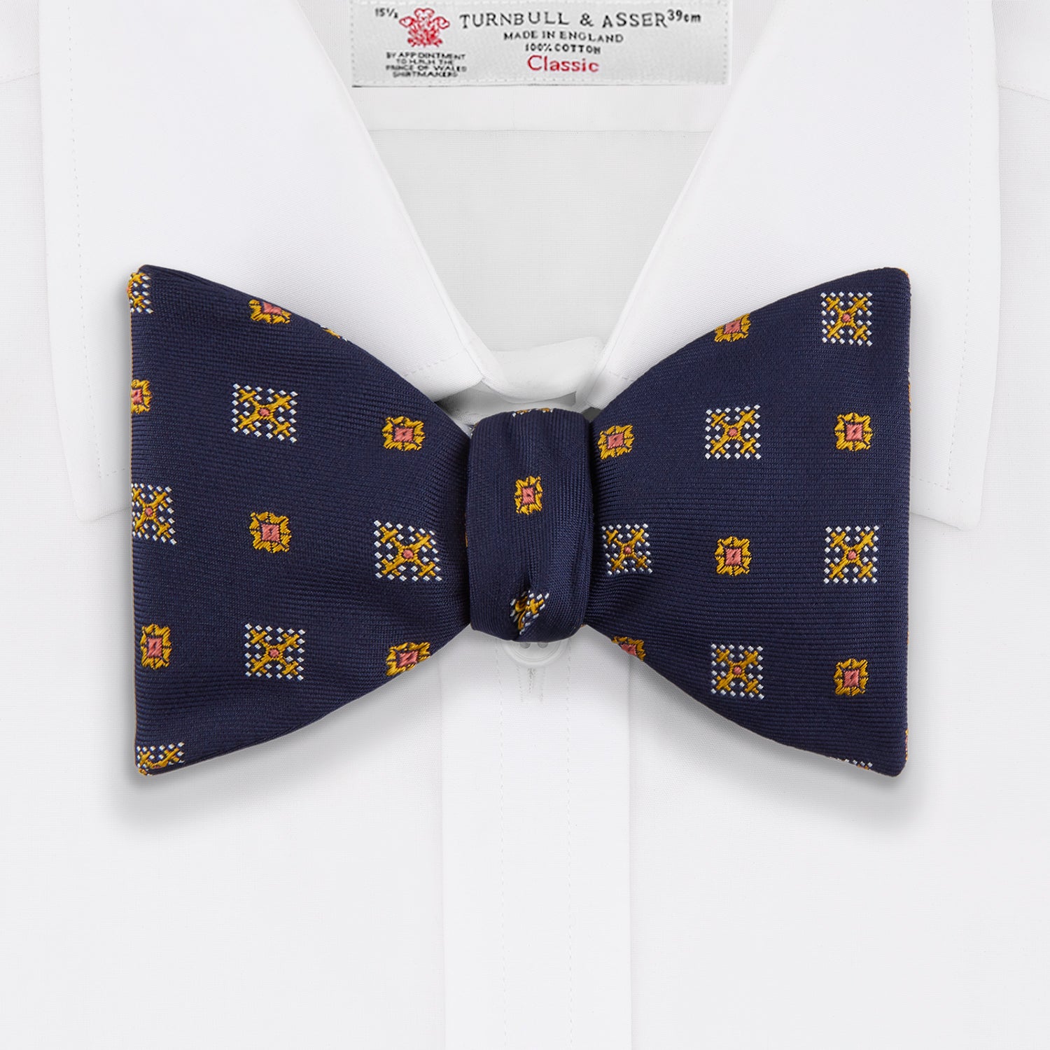 View 2 of product The Yellow Shields Bow Tie by Turnbull & Asser features a navy blue base with small yellow, orange, and white geometric squares, ideal for formal occasions and shown against a white background.
