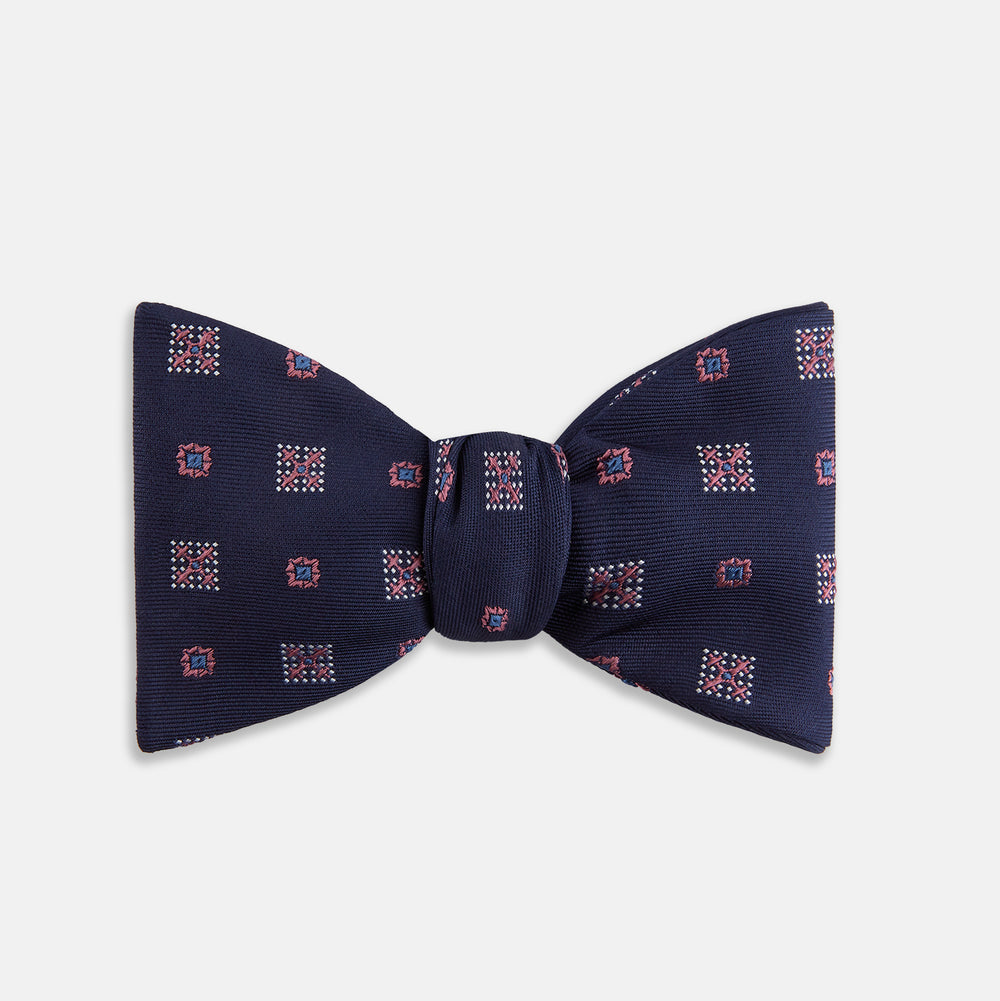The Turnbull & Asser Pink Shields Bow Tie features a pink pattern with shield motifs, ideal for formal occasions and displayed on a plain white background.