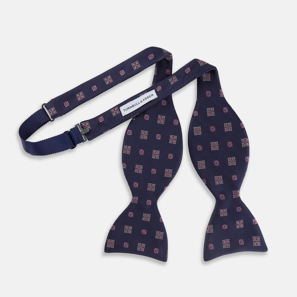 The Turnbull & Asser Pink Shields Bow Tie features a pink pattern with shield motifs, ideal for formal occasions and displayed on a plain white background.