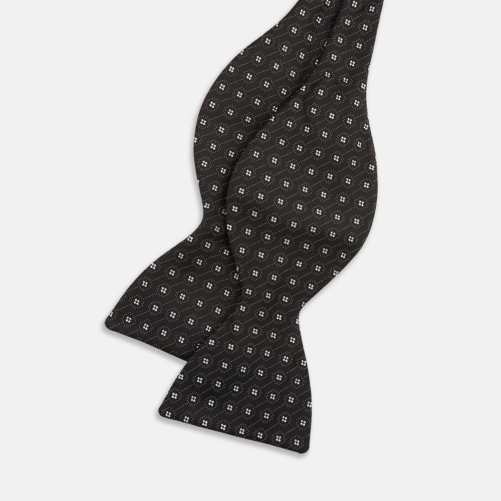 The Floral Piqué Monochrome Silk Bow Tie by Turnbull & Asser, featuring a repeating pattern of small white dots and hexagons on black silk, is ideal for formalwear or a dinner suit and is shown against a plain white background.