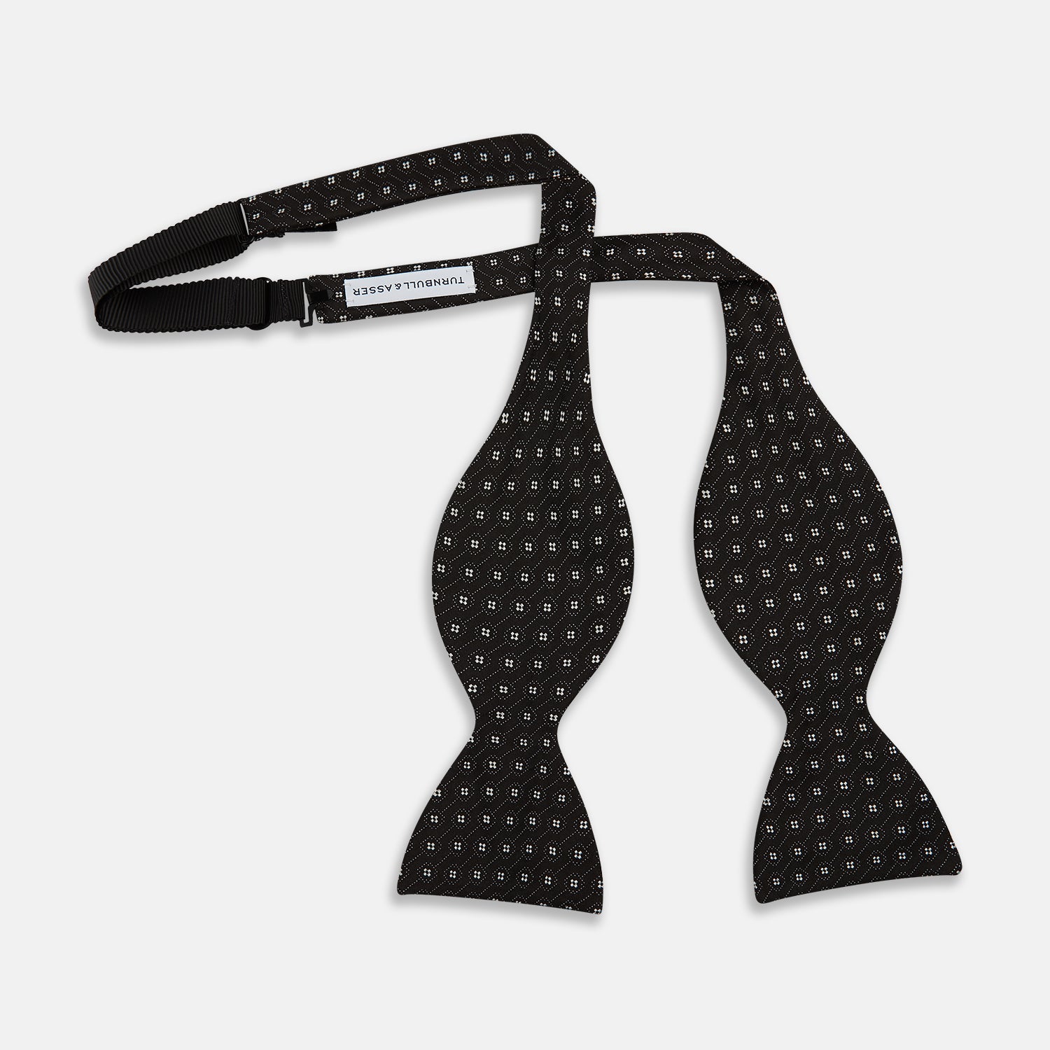 View 3 of product The Floral Piqué Monochrome Silk Bow Tie by Turnbull & Asser, featuring a repeating pattern of small white dots and hexagons on black silk, is ideal for formalwear or a dinner suit and is shown against a plain white background.