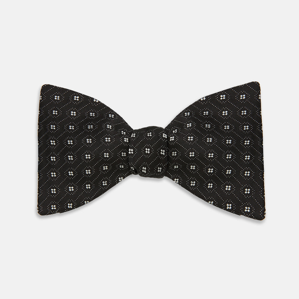 The Floral Piqué Monochrome Silk Bow Tie by Turnbull & Asser, featuring a repeating pattern of small white dots and hexagons on black silk, is ideal for formalwear or a dinner suit and is shown against a plain white background.