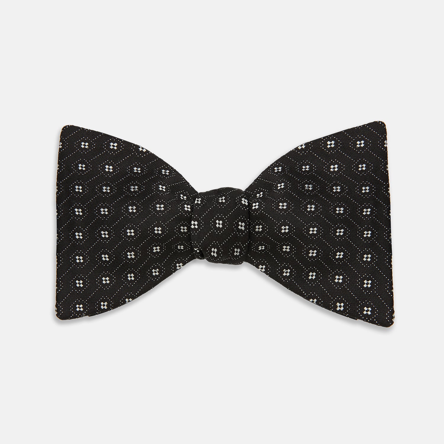 View 1 of product The Floral Piqué Monochrome Silk Bow Tie by Turnbull & Asser, featuring a repeating pattern of small white dots and hexagons on black silk, is ideal for formalwear or a dinner suit and is shown against a plain white background.
