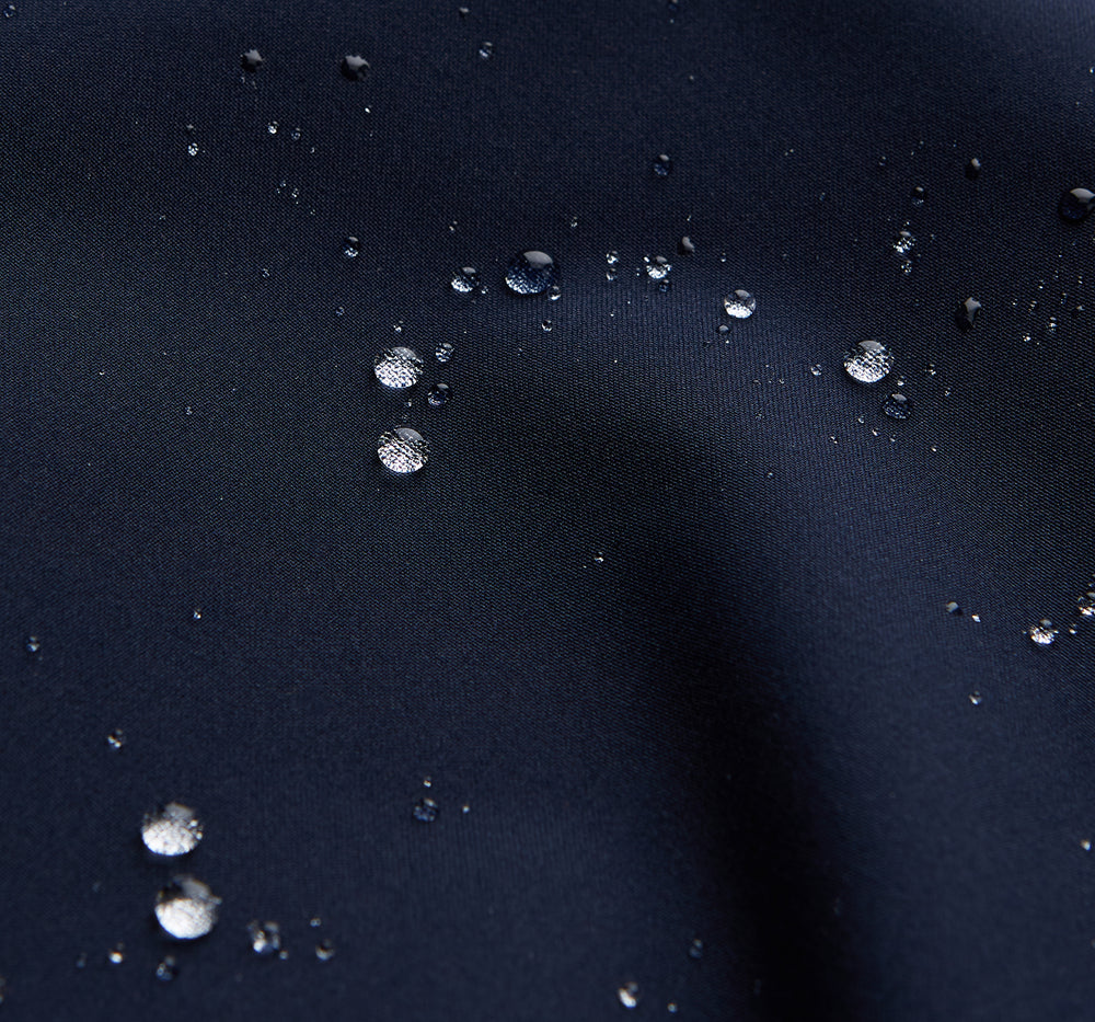 The Turnbull & Asser Navy Walter Sealup Parka with Detachable Liner features silver snap buttons, front flap pockets, and a drawstring hem. Styled against a white background, this waterproof parka offers both elegance and practicality for wet weather.