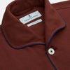 View 3 of product The Turnbull & Asser Red Cotton-Cashmere Pyjama Set features a rust-red long-sleeve button-up top with chest pocket and matching waist-tied pants, shown on a plain white background.
