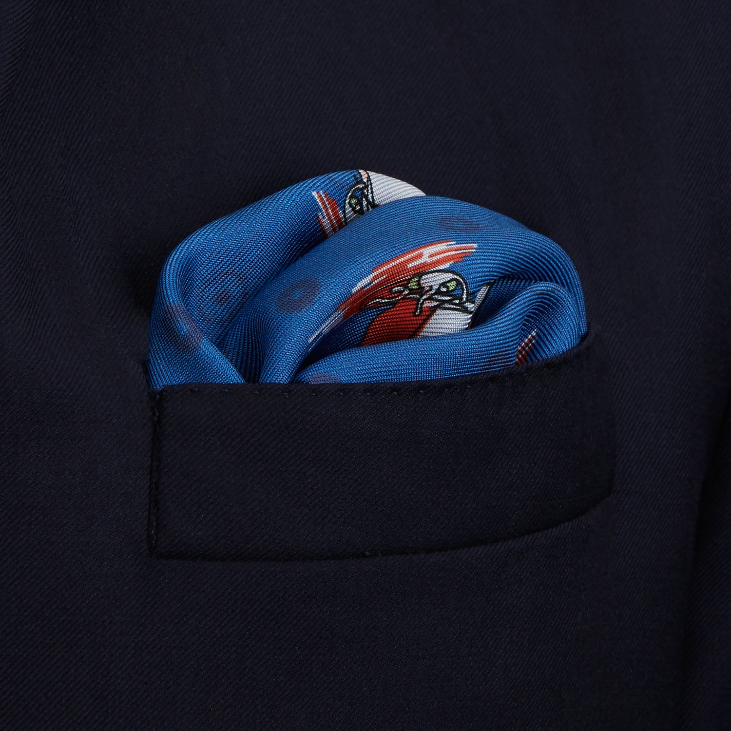 View 4 of product The Turnbull & Asser Blue Windsurfer Double-Faced Silk Print Pocket Square features a blue silk design with colorful windsurfers and vivid red edges, finished with the Turnbull & Asser logo in one corner.