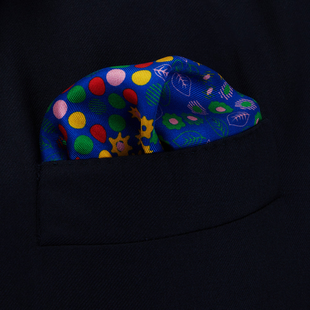 The Turnbull & Asser Navy Abstract Floral Silk Pocket Square features a vibrant blue base with colorful flowers, dots, and leaves arranged in a symmetrical geometric design for a sharp, tailored look.