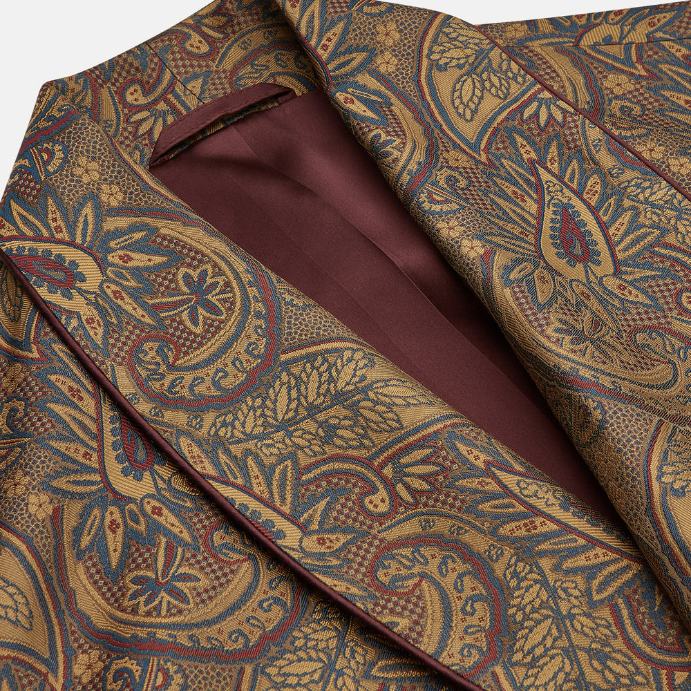 The Turnbull & Asser Gold Paisley Traditional Silk Jacquard Gown features a brown and gold paisley pattern, shawl collar, front pockets, and matching fabric belt. Displayed on a white background, it’s perfect for winter comfort.