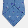 View 4 of product The Blue Multi Floral Motif Silk Tie by Turnbull & Asser features subtle diagonal stripes and blue and white floral medallions on light blue silk—ideal for bold shirts. The tie is shown rolled at one end.