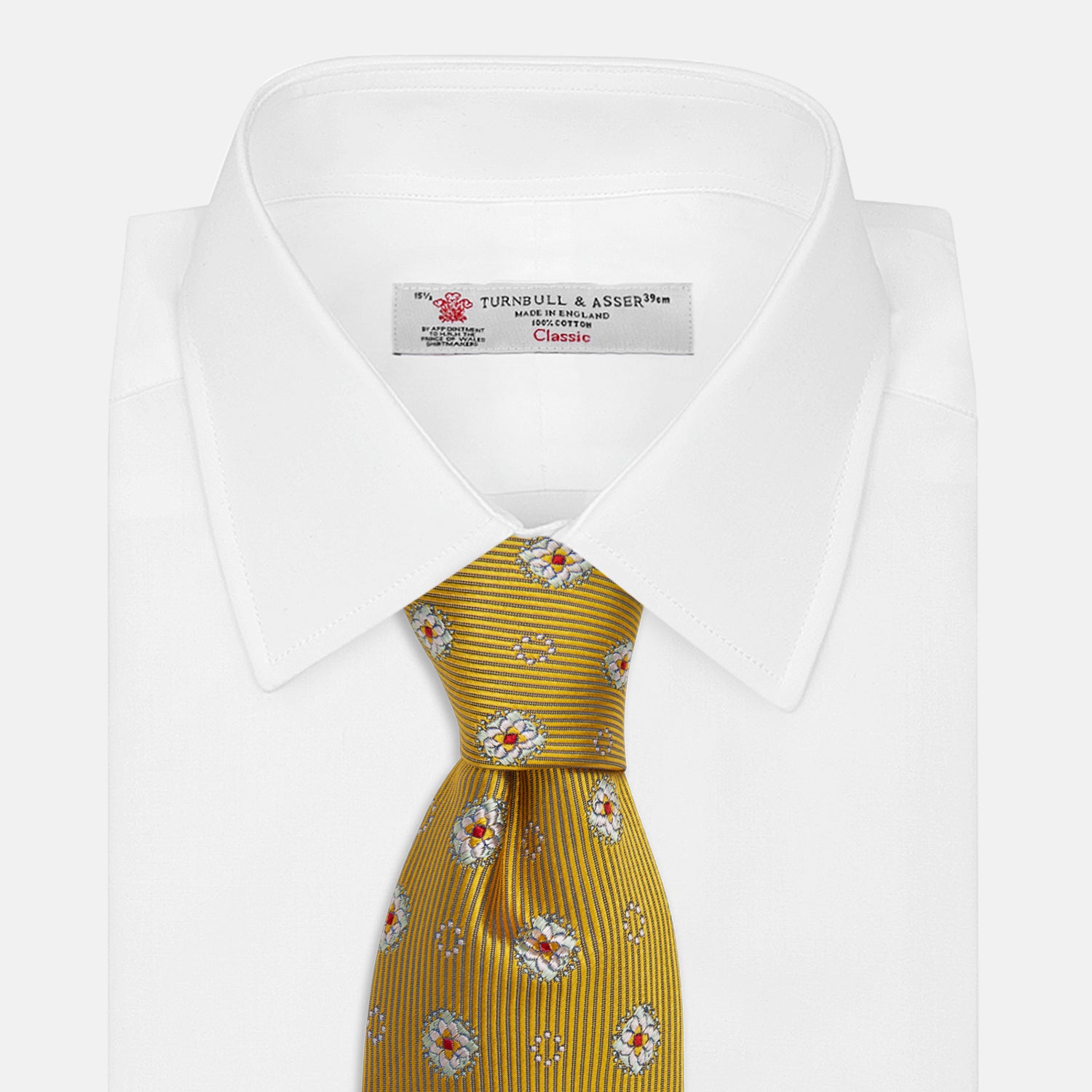 View 2 of product The Yellow Multi Floral Motif Silk Tie by Turnbull & Asser features subtle diagonal stripes and small white, blue, and orange floral motifs—a perfect summer palette, shown rolled up on a plain white background.