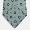 View 4 of product The Green Multi Floral Motif Silk Tie by Turnbull & Asser features light gray silk with thin diagonal stripes and a floral medallion pattern in pink, purple, and green—ideal for adding summer color to your outfit. Displayed rolled up on a white background.