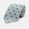 View 1 of product The Green Multi Floral Motif Silk Tie by Turnbull & Asser features light gray silk with thin diagonal stripes and a floral medallion pattern in pink, purple, and green—ideal for adding summer color to your outfit. Displayed rolled up on a white background.