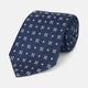 The Turnbull & Asser Navy Floral Emblem Tie displays a repeating pattern of small light blue, white, and yellow floral and diamond motifs, highlighting refined elegance, shown rolled up on a white background.