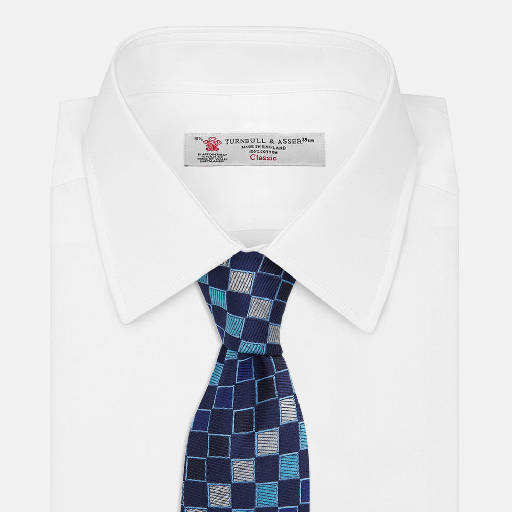 The Blue Multi Check Silk Tie by Turnbull & Asser features a geometric checked pattern in blue, light blue, and silver on dark navy—ideal for pairing with bold shirts.