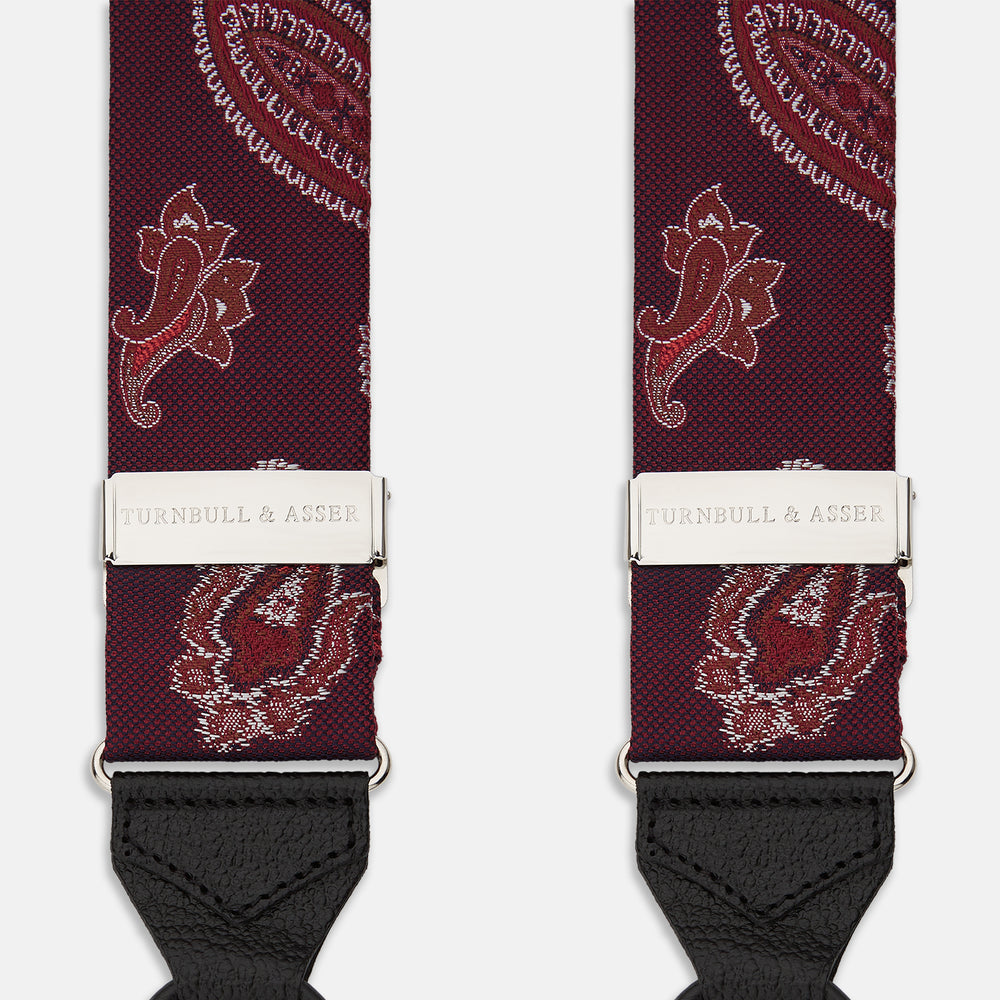 Two red paisley adjustable silk braces by Turnbull & Asser, featuring leather ends and silver clasps, are laid out vertically side by side on a white background.