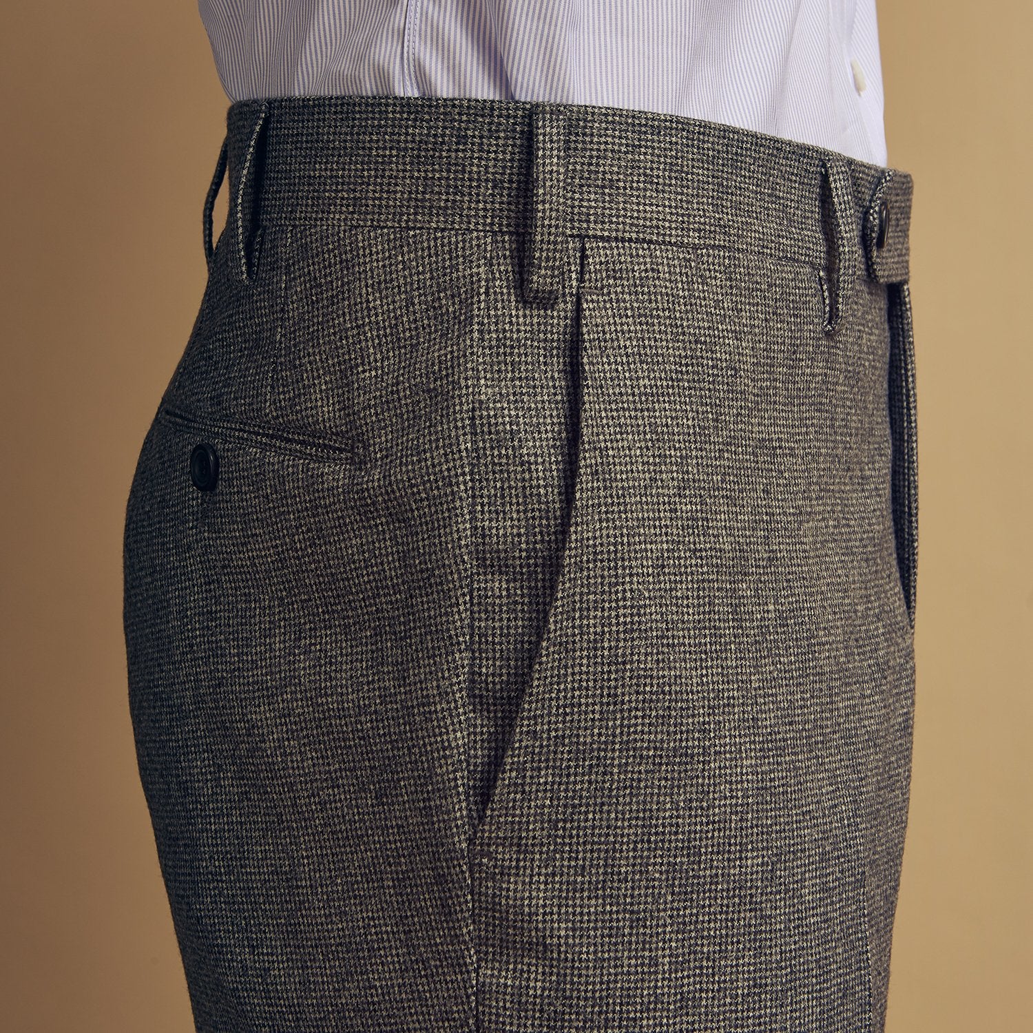 View 5 of product A person wears Turnbull & Asser Grey Puppytooth Wool Manson Trousers, a white dress shirt with rolled-up sleeves, and black shoes, standing against a plain beige background.