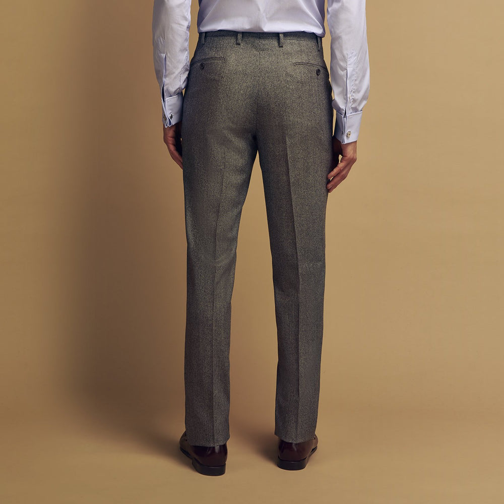 A person wears Turnbull & Asser Grey Puppytooth Wool Manson Trousers, a white dress shirt with rolled-up sleeves, and black shoes, standing against a plain beige background.