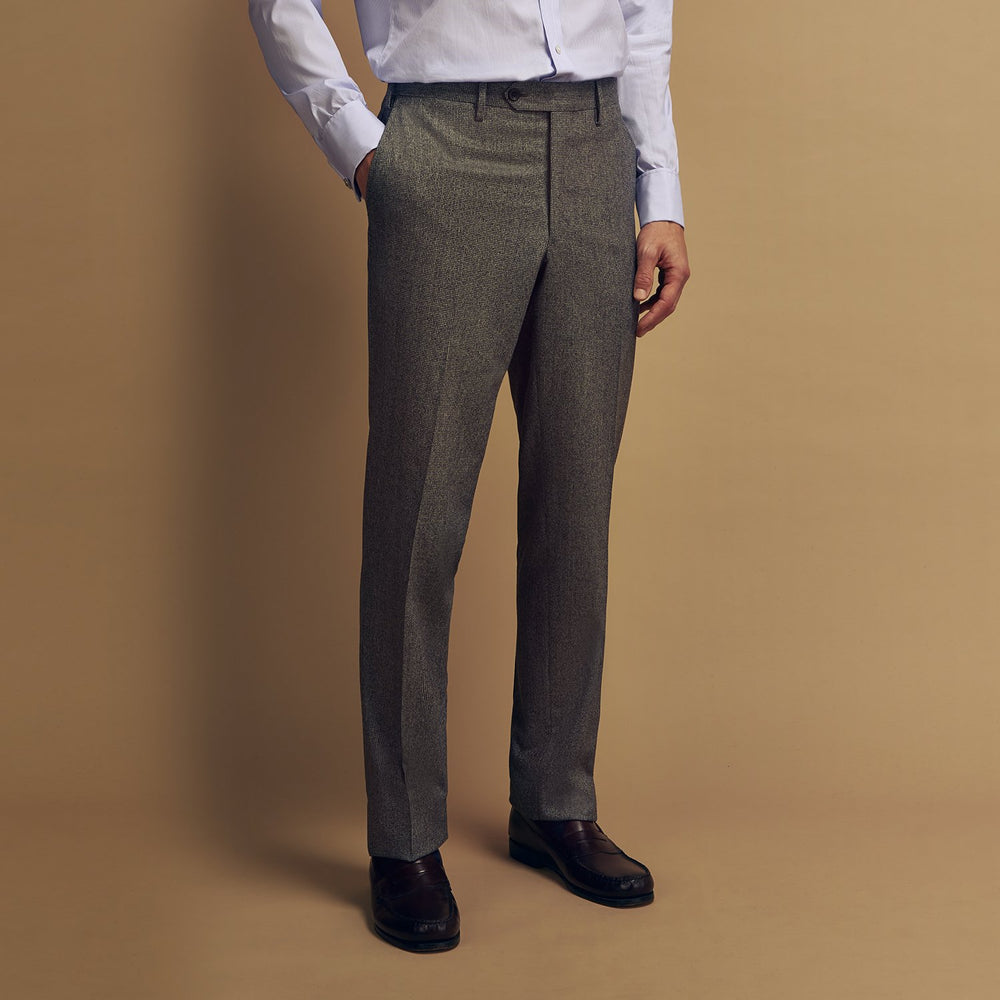 A person wears Turnbull & Asser Grey Puppytooth Wool Manson Trousers, a white dress shirt with rolled-up sleeves, and black shoes, standing against a plain beige background.