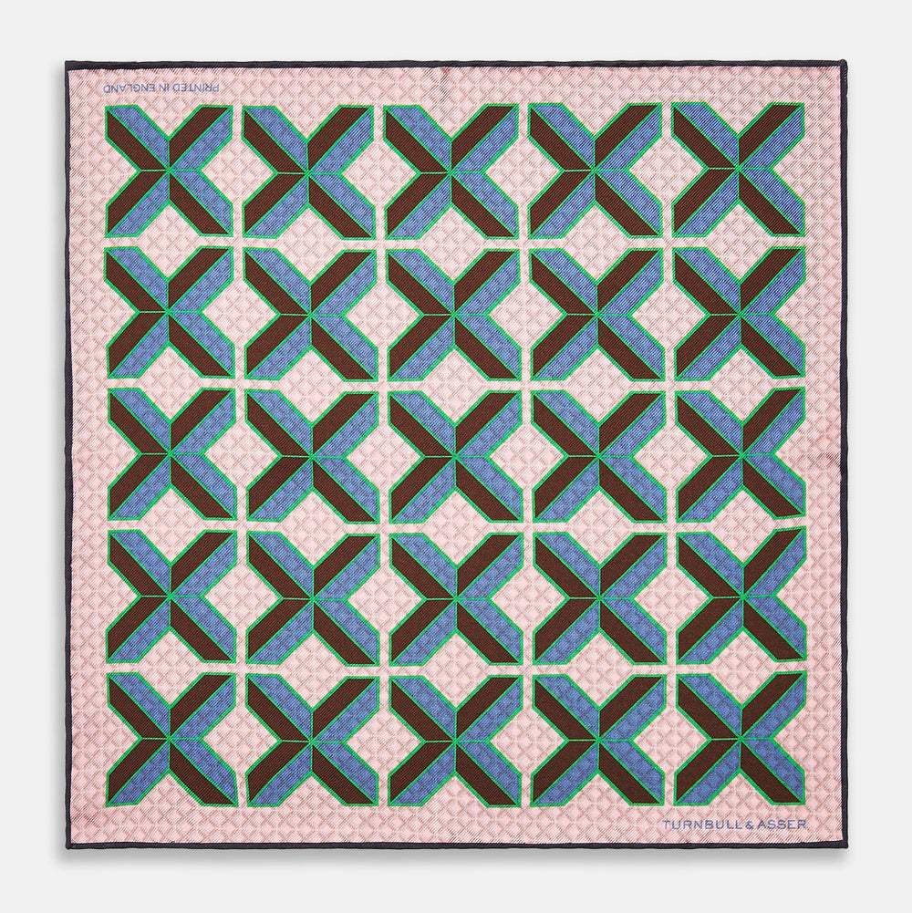 The Pink Multi Crosses Double-Faced Silk Pocket Square by Turnbull & Asser features blue, green, and brown interlocking X-shaped graphics on light pink, with OSINACHI X CJANGO and TURNBULL & ASSER printed at the corners.
