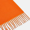 View 2 of product The Turnbull & Asser Orange Purled Fringe Cashmere Scarf is shown neatly arranged on a white background, featuring soft, thick cashmere with fringe at both ends and a subtle embroidered logo near one edge.