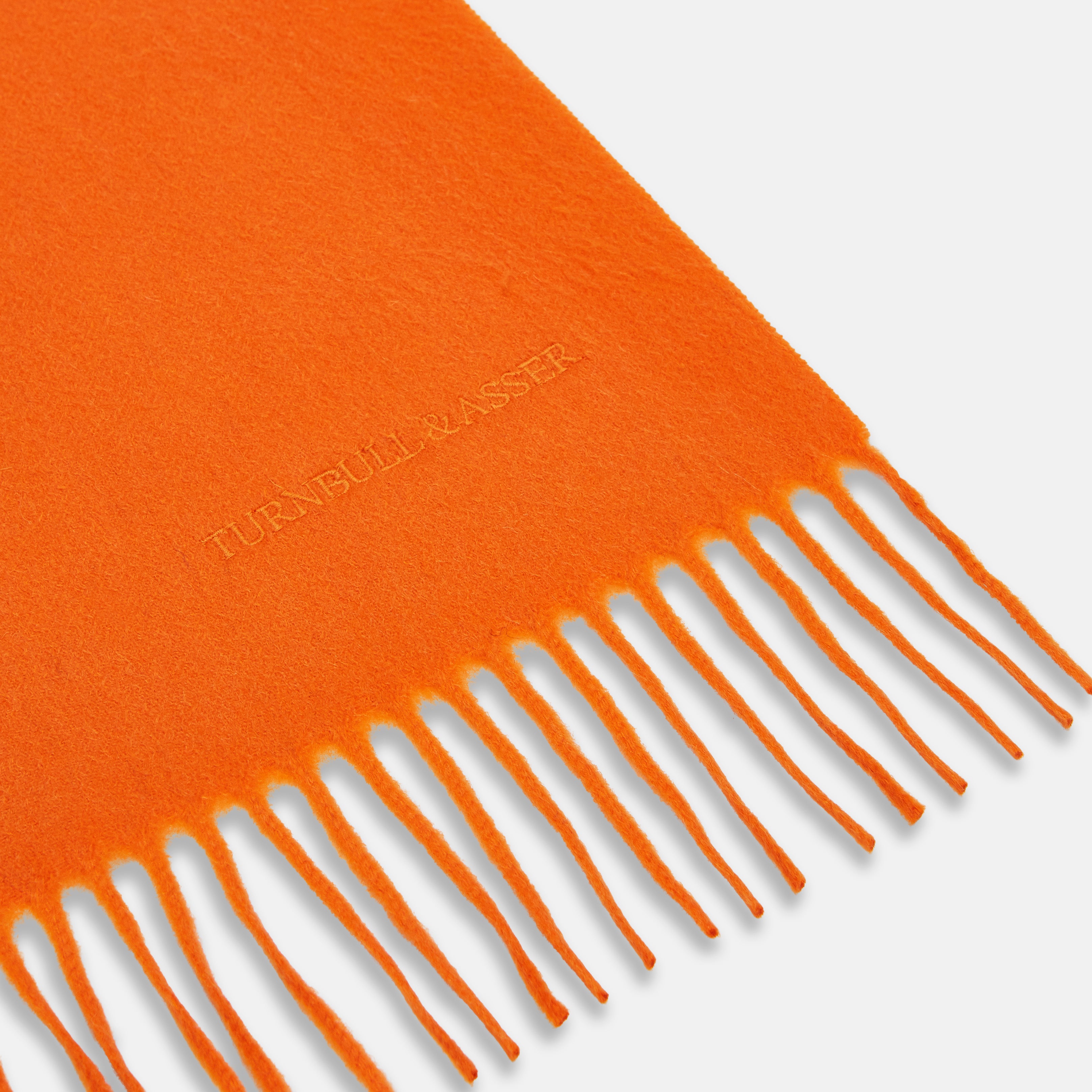 View 2 of product The Turnbull & Asser Orange Purled Fringe Cashmere Scarf is shown neatly arranged on a white background, featuring soft, thick cashmere with fringe at both ends and a subtle embroidered logo near one edge.