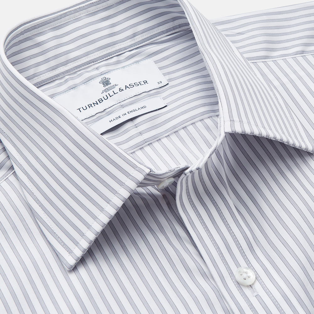 A man wearing the Turnbull & Asser Grey Multi Stripe Regular Fit Twill Shirt with T&A Collar and Double Cuffs stands against a beige background, one hand in his pocket, looking at the camera.