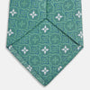 View 4 of product The Turnbull & Asser Green Multi Neat Silk Tie, handmade and featuring a white and light blue geometric pattern, is shown rolled up on a plain white background.