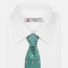 View 2 of product The Turnbull & Asser Green Multi Neat Silk Tie, handmade and featuring a white and light blue geometric pattern, is shown rolled up on a plain white background.
