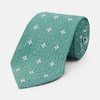 View 1 of product The Turnbull & Asser Green Multi Neat Silk Tie, handmade and featuring a white and light blue geometric pattern, is shown rolled up on a plain white background.