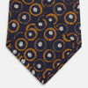 View 4 of product The Turnbull & Asser Orange Multi Circle Printed Silk Tie features navy blue silk with orange circles and white ovals, perfect for elevating any formal outfit. Shown on a plain white background.