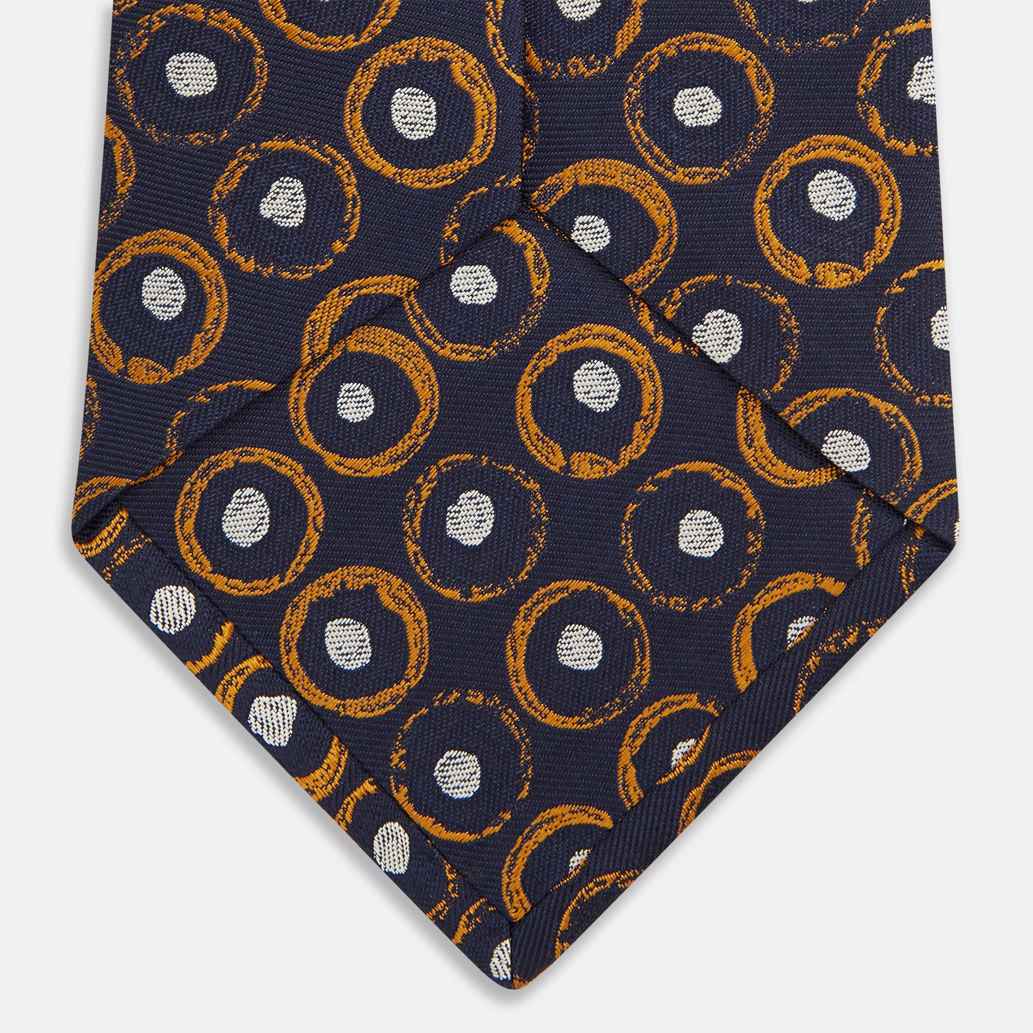 View 4 of product The Turnbull & Asser Orange Multi Circle Printed Silk Tie features navy blue silk with orange circles and white ovals, perfect for elevating any formal outfit. Shown on a plain white background.
