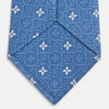 View 4 of product The Blue Multi Neat Silk Tie by Turnbull & Asser features a geometric pattern of white four-pointed shapes and circles, crafted in blue silk from the autumn-winter collection. Displayed rolled on a plain light background.