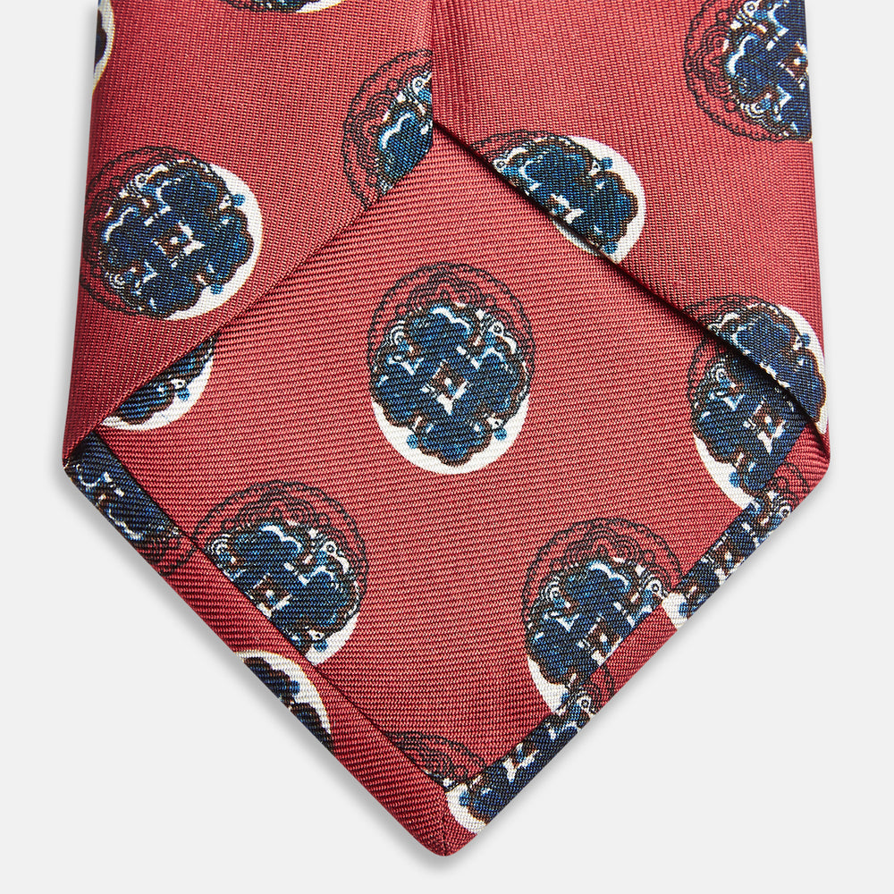 A rolled-up Red Shadow Spot Printed Silk Tie by Turnbull & Asser, showcasing large navy blue and white circular motifs, displayed on a plain white background.