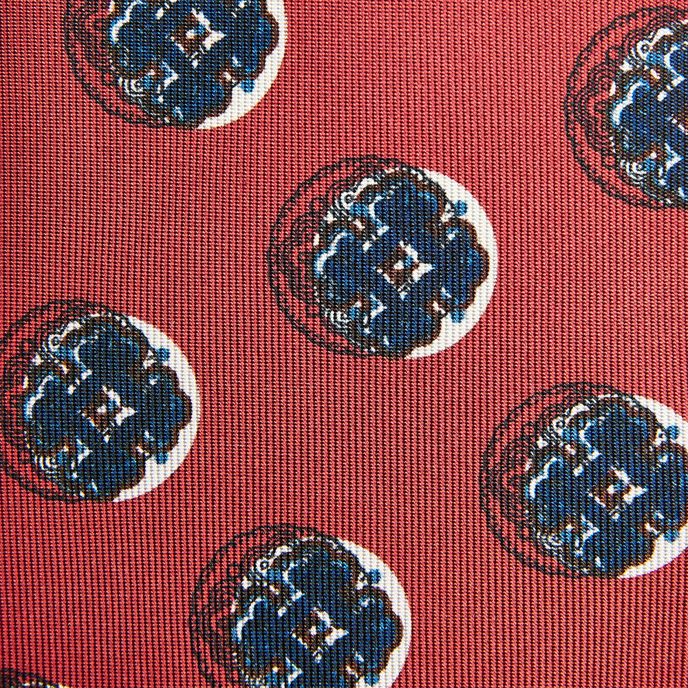 A rolled-up Red Shadow Spot Printed Silk Tie by Turnbull & Asser, showcasing large navy blue and white circular motifs, displayed on a plain white background.