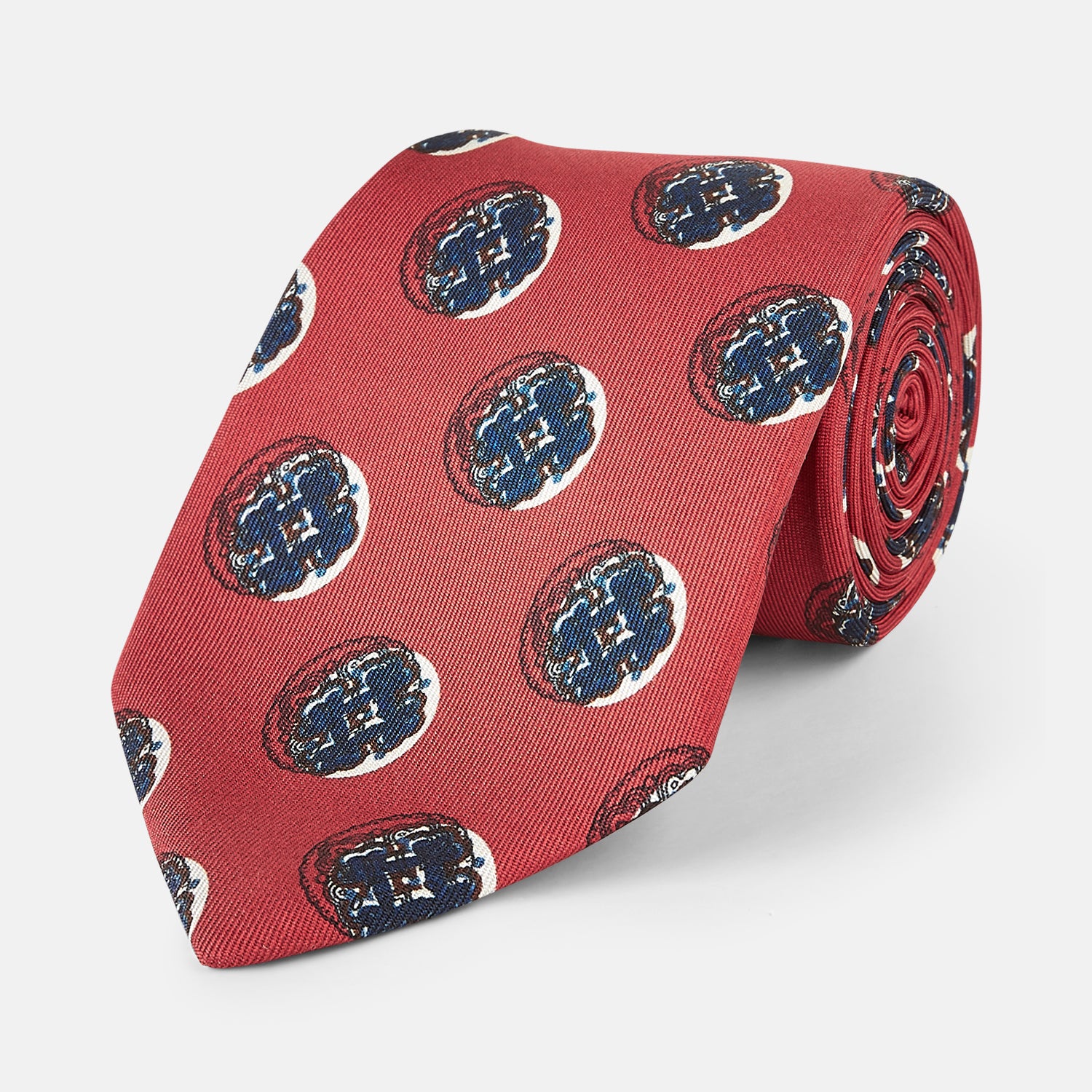 View 1 of product A rolled-up Red Shadow Spot Printed Silk Tie by Turnbull & Asser, showcasing large navy blue and white circular motifs, displayed on a plain white background.