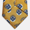 View 4 of product A rolled-up Turnbull & Asser Gold Shadow Spot Printed Silk Tie, featuring blue and white circular patterns on fine Adamley Macclesfield silk, displayed against a white background.