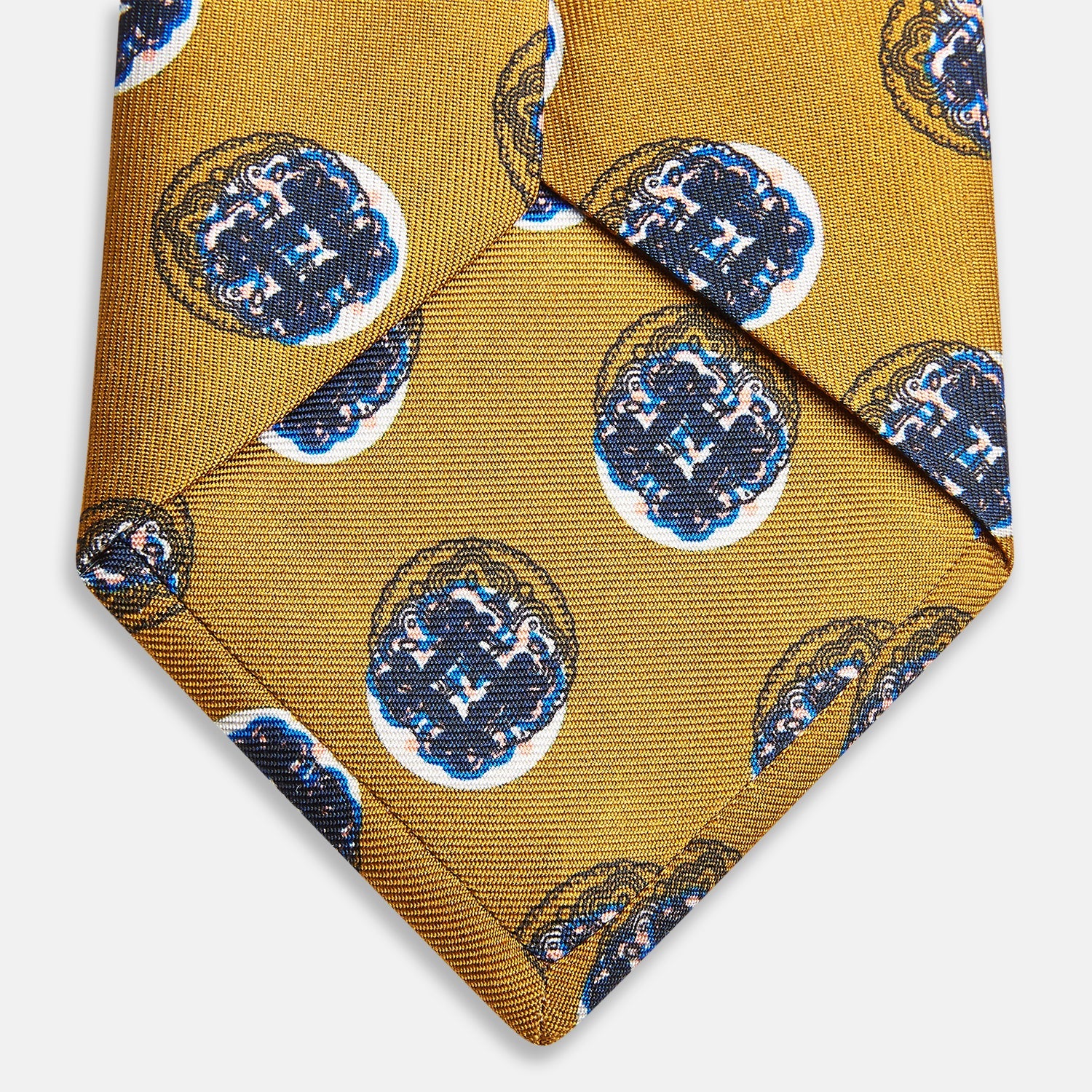 View 4 of product A rolled-up Turnbull & Asser Gold Shadow Spot Printed Silk Tie, featuring blue and white circular patterns on fine Adamley Macclesfield silk, displayed against a white background.
