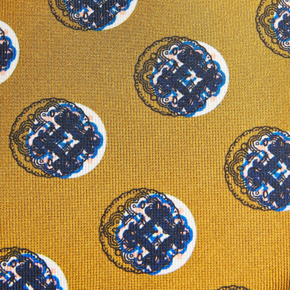 A rolled-up Turnbull & Asser Gold Shadow Spot Printed Silk Tie, featuring blue and white circular patterns on fine Adamley Macclesfield silk, displayed against a white background.