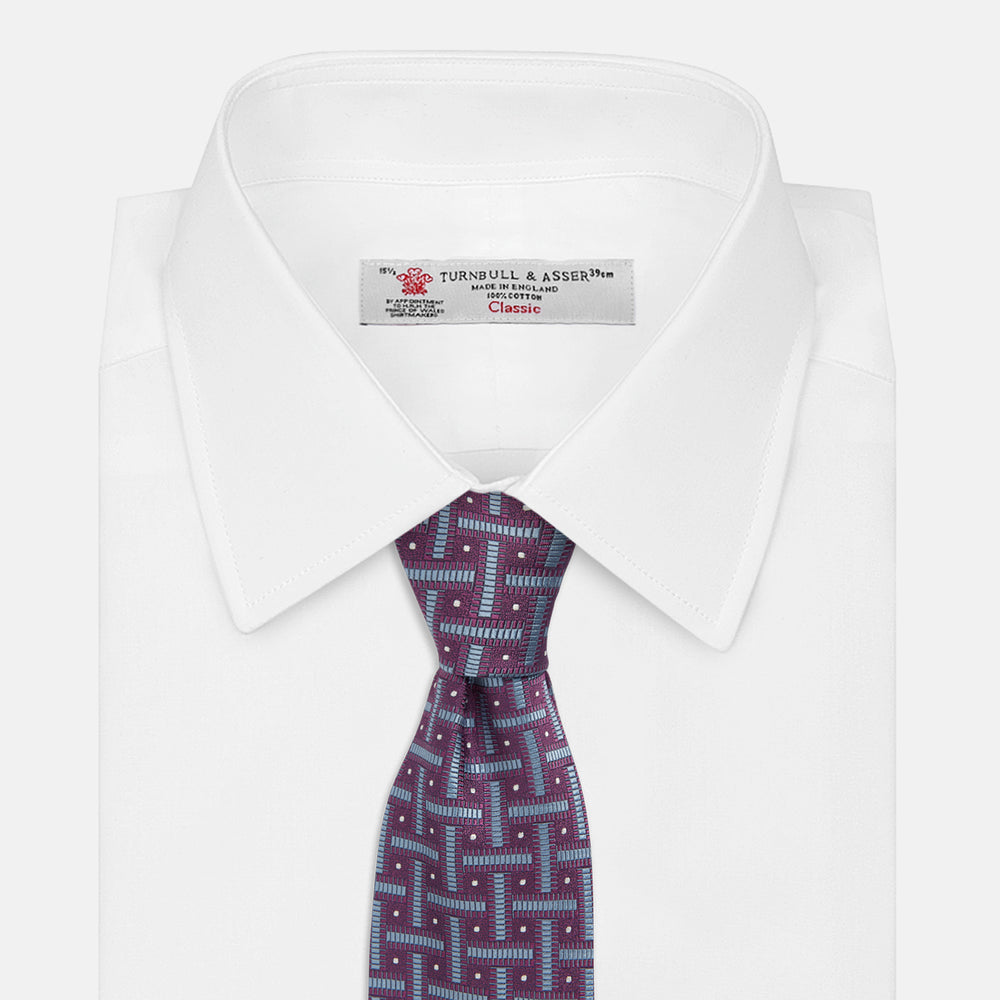 The Turnbull & Asser Purple & Navy Cross Silk Tie features a geometric pattern of intersecting blue lines and white dots—an ideal accessory to elevate formal outfits or complement signature shirts.