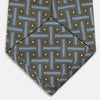 View 4 of product The Turnbull & Asser Green & Navy Cross Silk Tie features an olive green base with navy geometric patterns and white dots, shown rolled on a light surface—an ideal accessory to elevate any formal look.