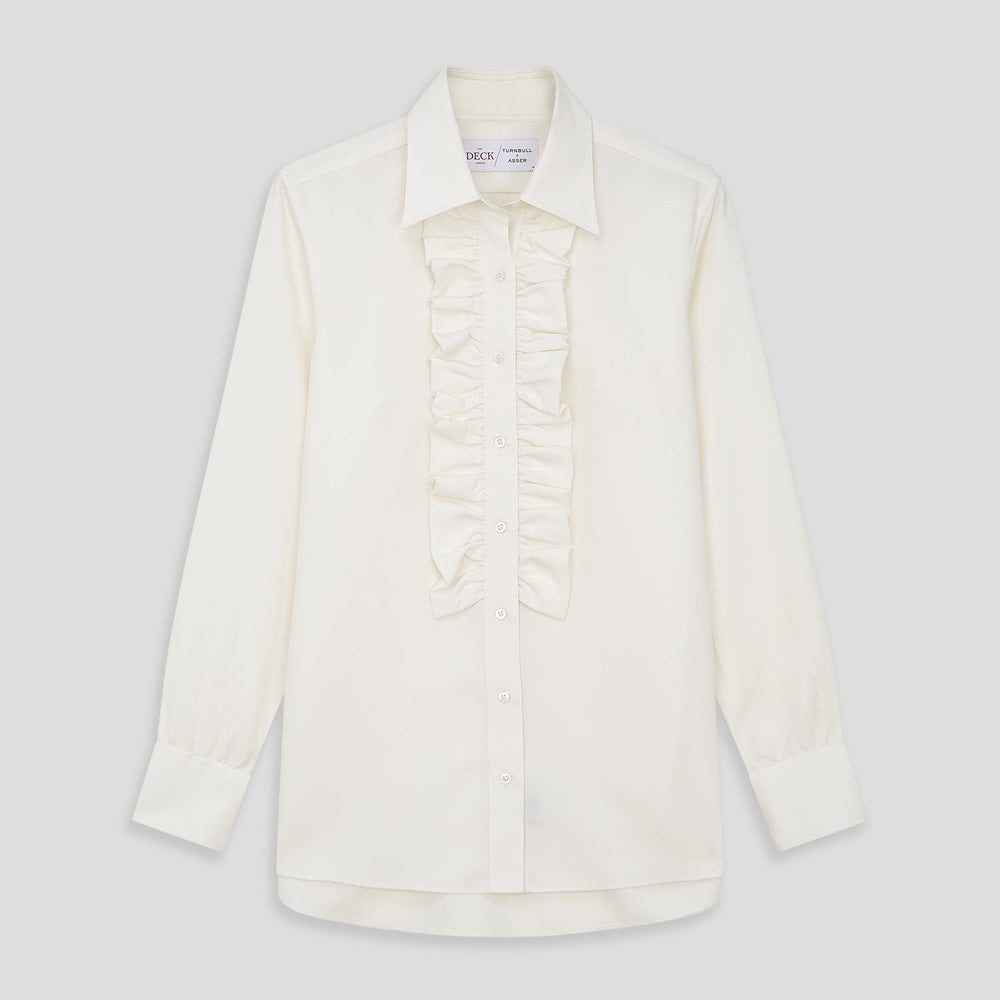 The Turnbull & Asser Turnbull and The Deck Cream Silk Romantic Shirt features long sleeves, a pointed collar, and elegant front ruffles, shown against a plain light gray background.