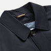 View 3 of product A man with brown hair stands outdoors, hands in his pockets, wearing a Turnbull & Asser Navy Sealup Quilted Liner Quintern Car Coat over a mustard cardigan. A glass barrier and blurred background are behind him.