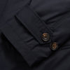 View 4 of product A man with brown hair stands outdoors, hands in his pockets, wearing a Turnbull & Asser Navy Sealup Quilted Liner Quintern Car Coat over a mustard cardigan. A glass barrier and blurred background are behind him.