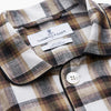 View 4 of product The Turnbull & Asser Brown Multi Check Linen Hyde Pyjama Set features a button-up, long-sleeve top and pants with a brown, black, and white plaid pattern, shown on a white background.